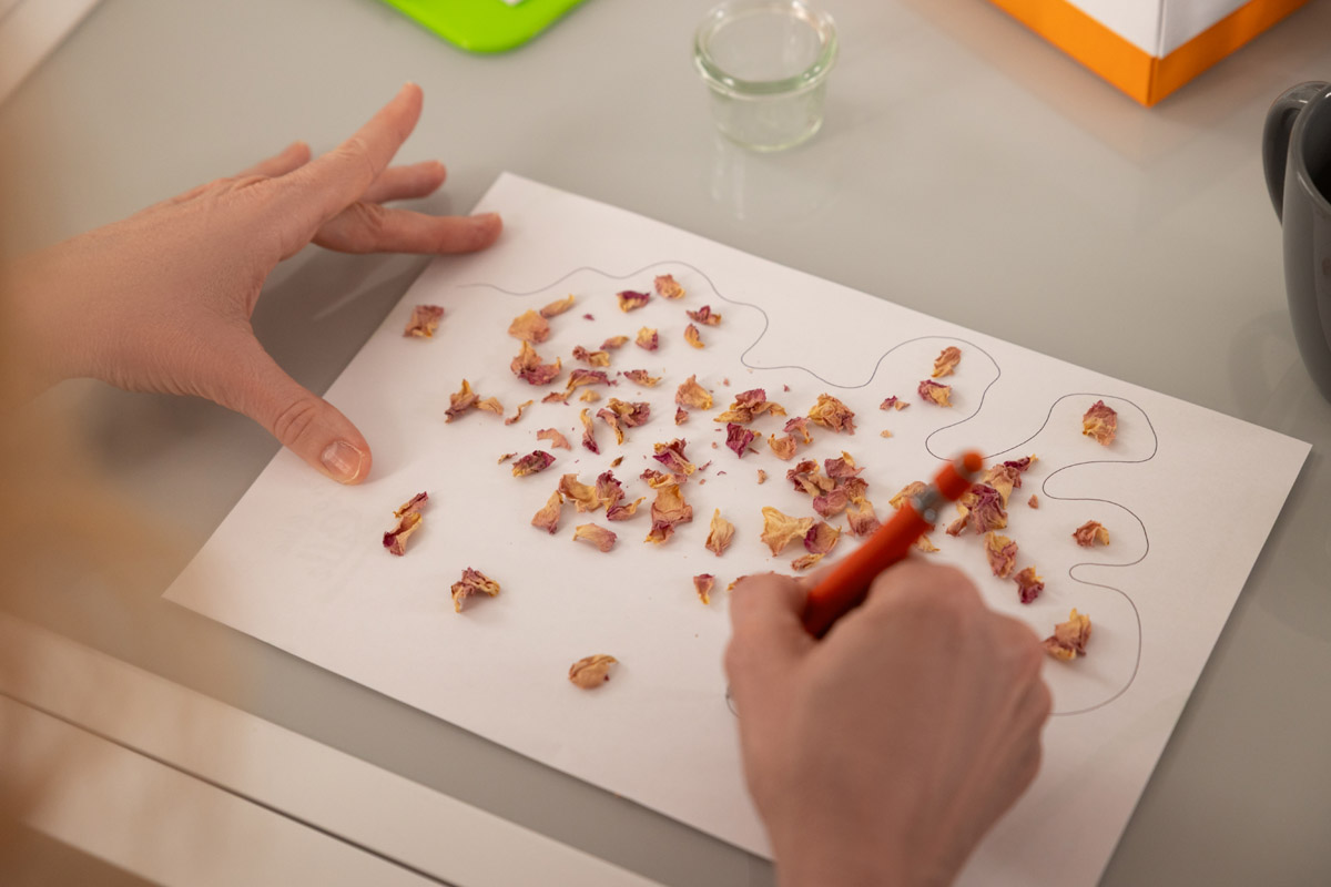 A participant’s draws an outline around strewn rose petals on a piece of paper.